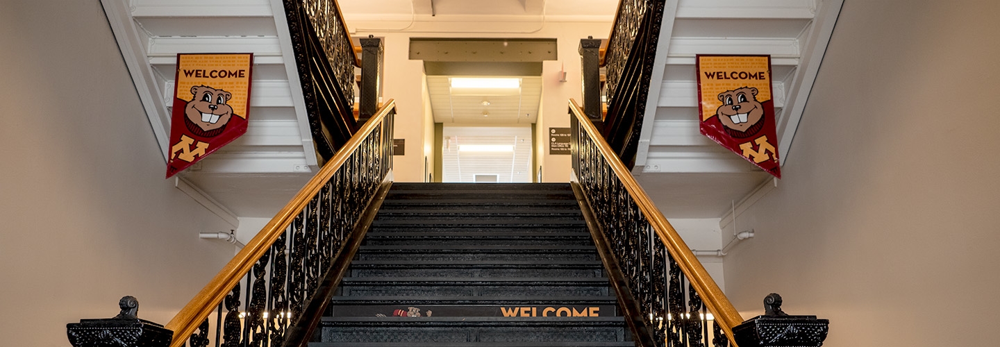 Upward view of main staircase in Jones Hall, with welcome banners of Goldy the Gopher hanging on both sides of the stairs.