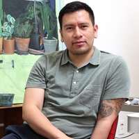 A Latinx man wearing polo shirt sits at a painting easel